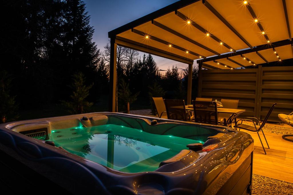 The same hot tub at night, teal jets glowing under warm string lights on the pergola